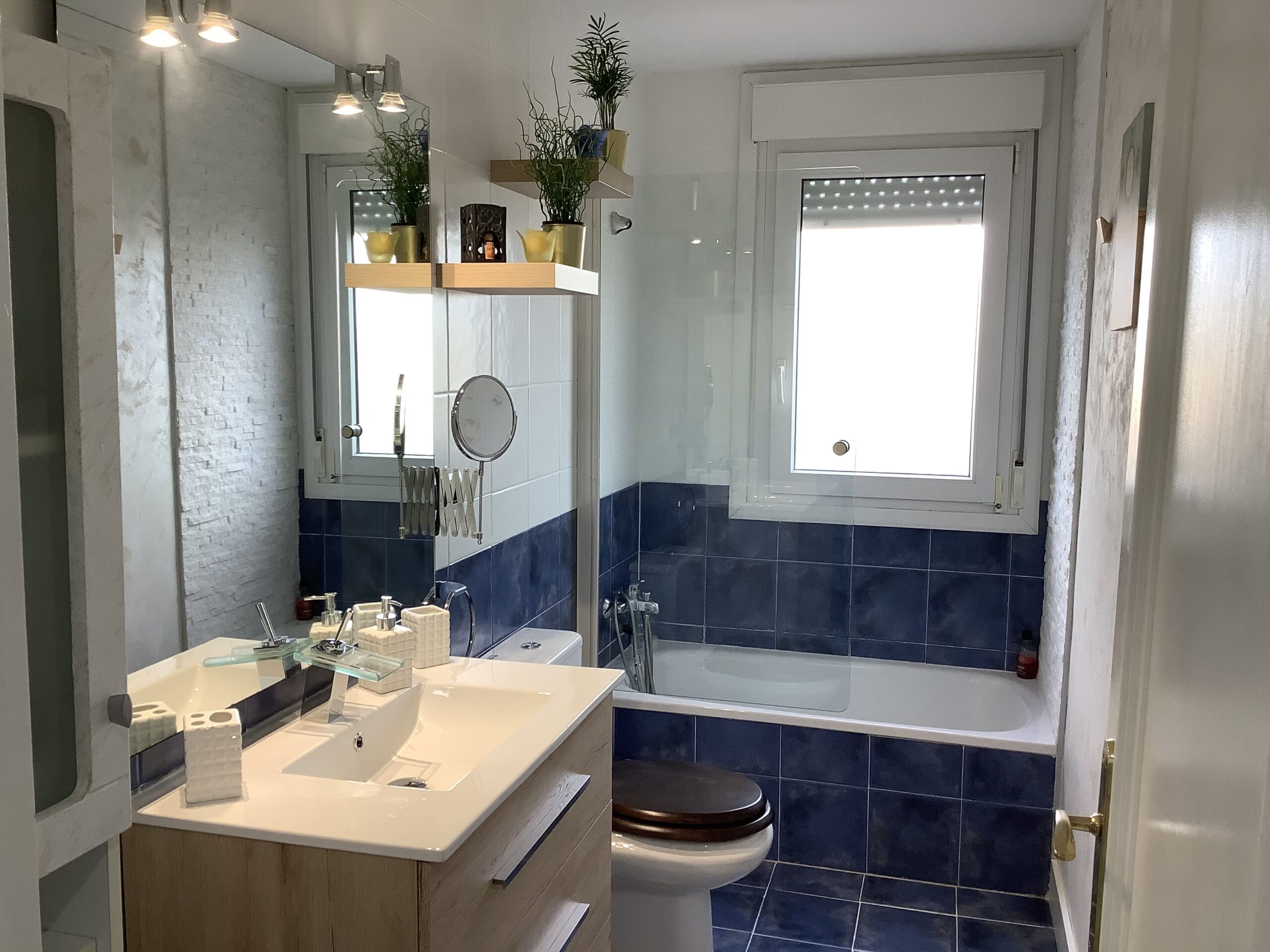 Después: Baño reformado con mueble de madera y espejo. Antes: baño antiguo con azulejos azules y bañera.