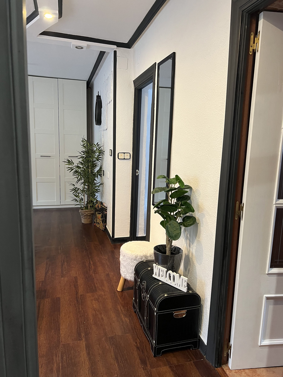 Después: Pasillo con suelo de madera y plantas decorativas. Antes: pasillo en obra con paredes sin pintar.