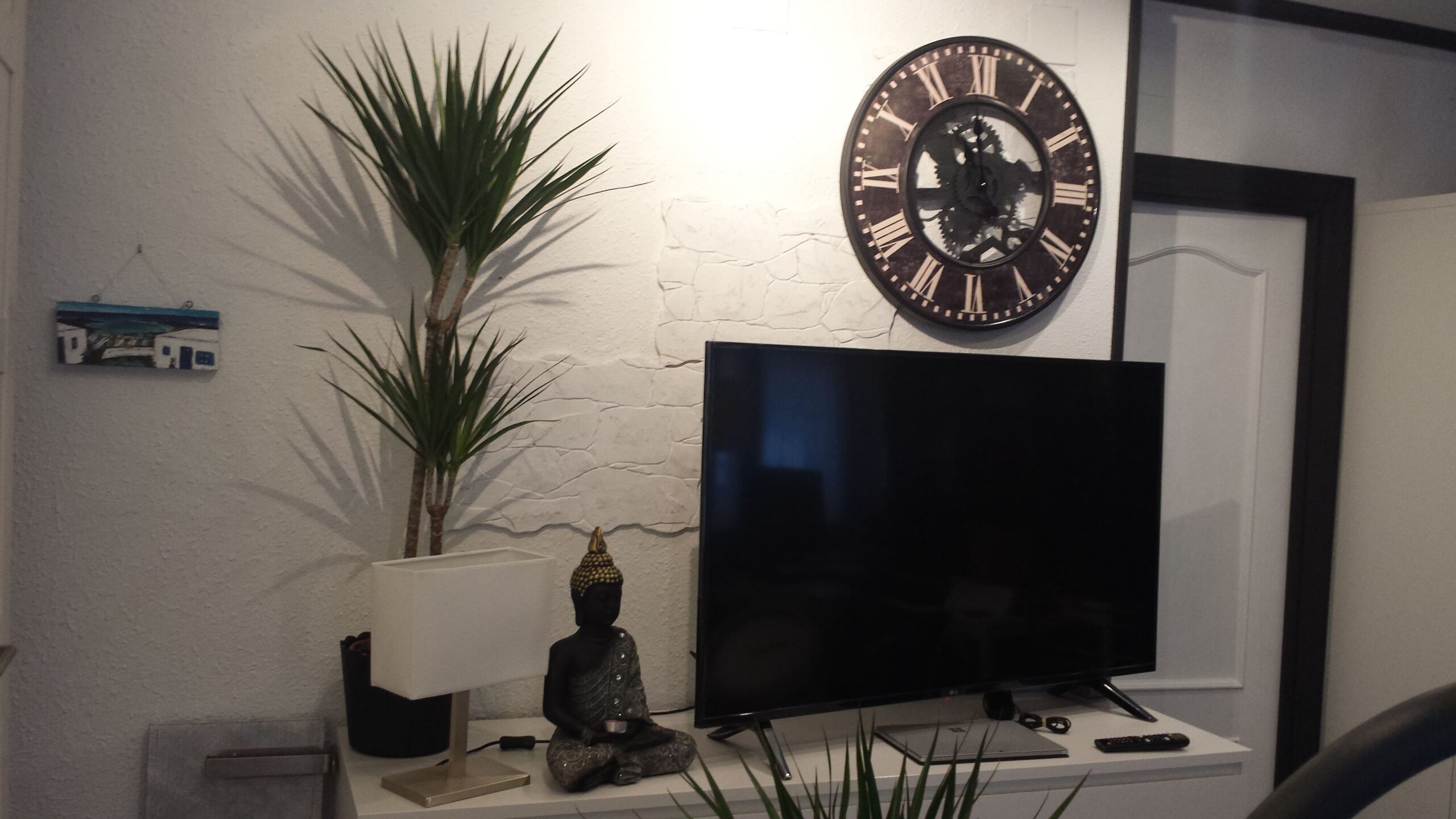 Después: Salón con mueble de TV, reloj de pared y plantas. Antes: salón con pared fucsia.