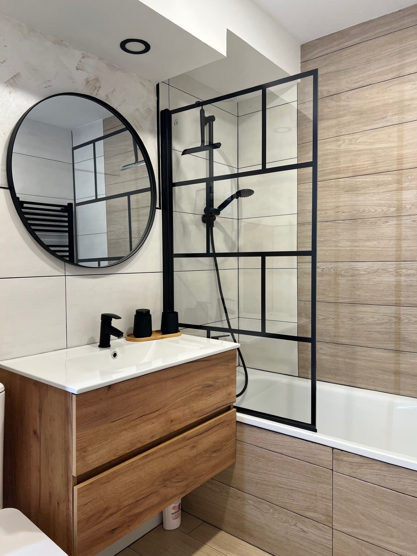 Después: Baño con mampara negra, espejo redondo y mueble de madera. Antes: espacio en obra.