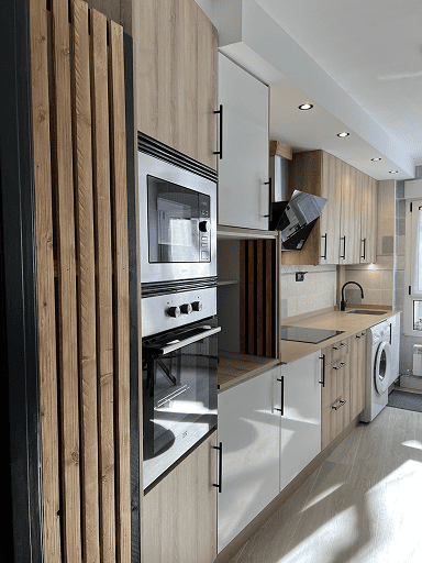 Cocina con columna de horno, lamas de madera y muebles blancos