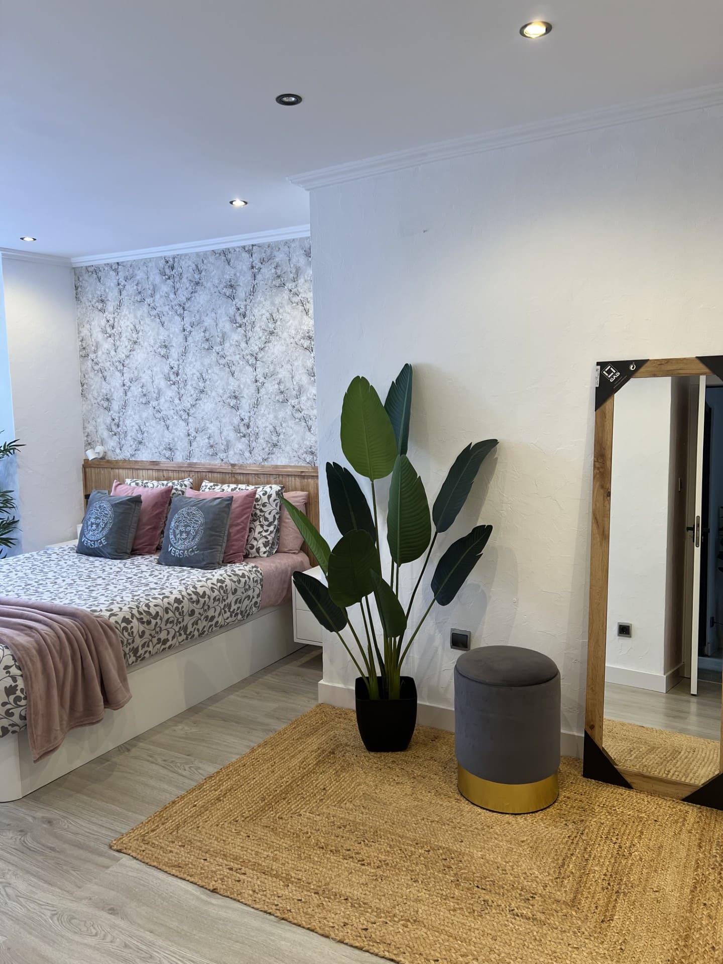 Después: Dormitorio con papel pintado floral, espejo de pie y planta. Antes: dormitorio en obra con pared sin terminar.