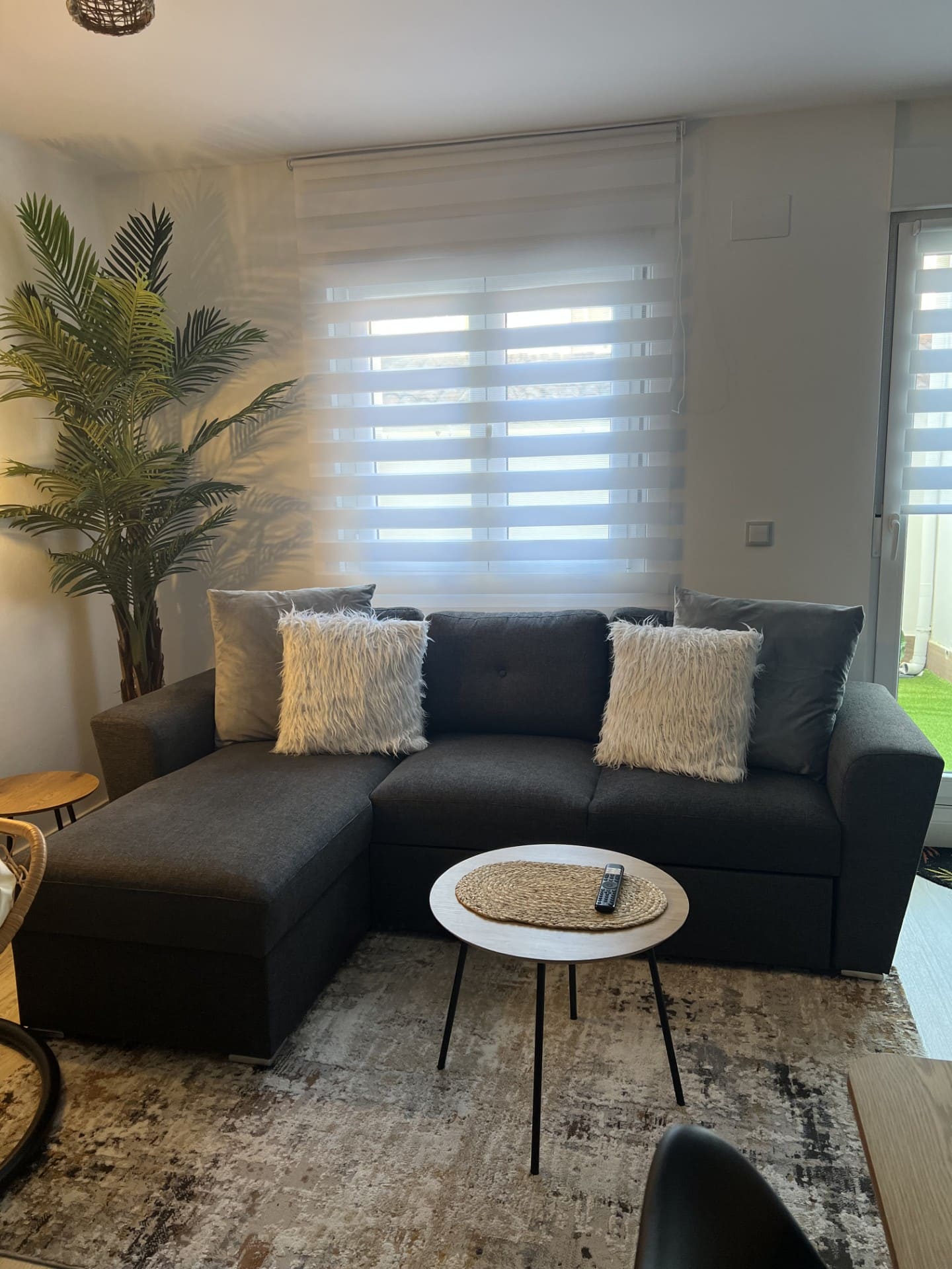 Después: Salón con sofá negro, cojines y mesa de centro blanca. Antes: salón desordenado y sin decorar.